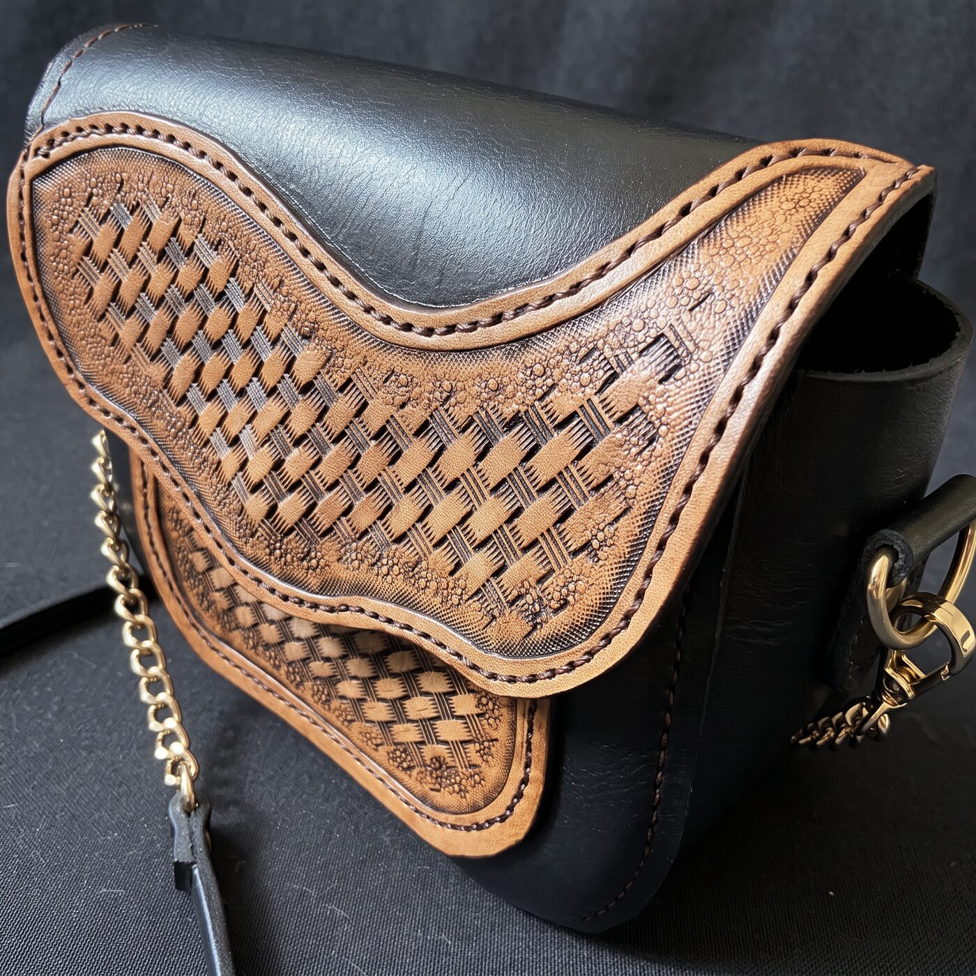 Hand-tooled crossbody bag in black leather with caramel basketweave overlays and a gold chain strap